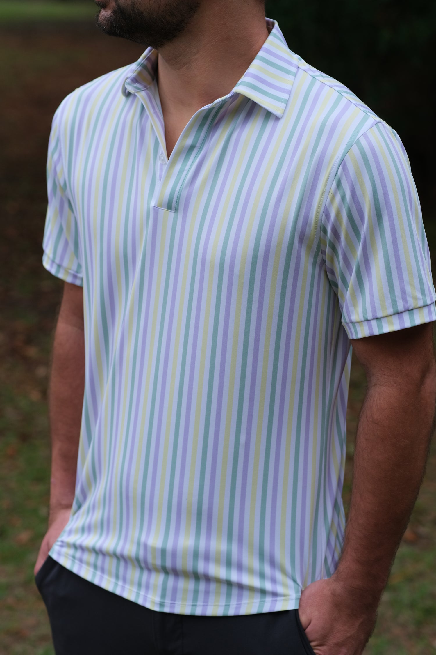 A man wearing a polo shirt that is white with yelow, purple, and green pastel stripes.